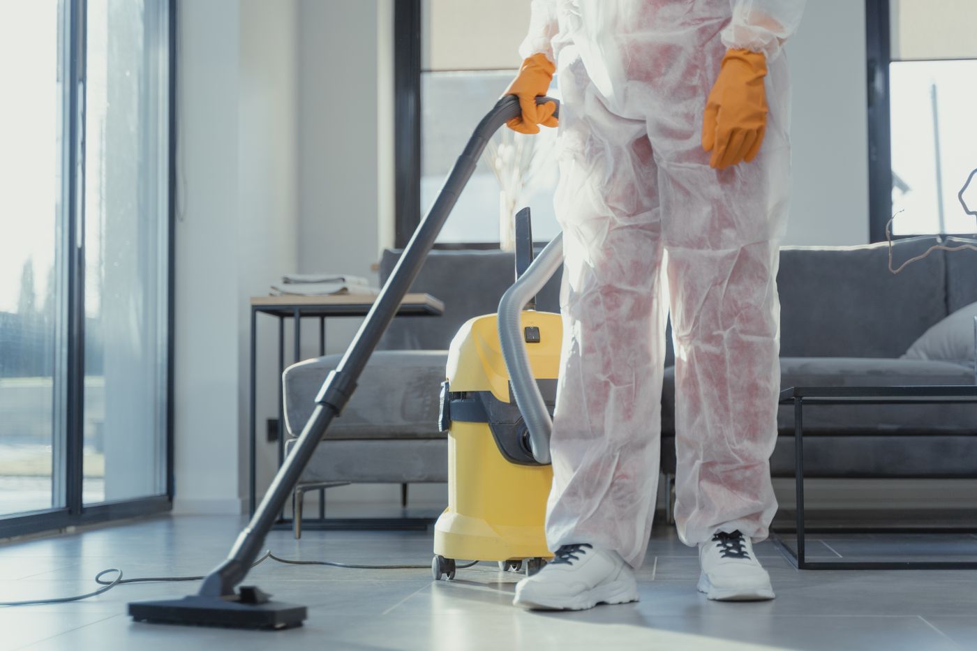 Nettoyeur en combinaison aspirant un salon après travaux